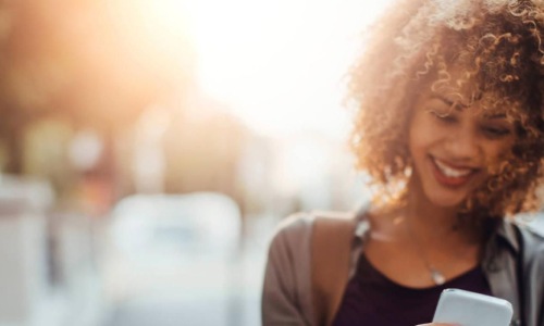 woman texts on her phone as she walks through the city